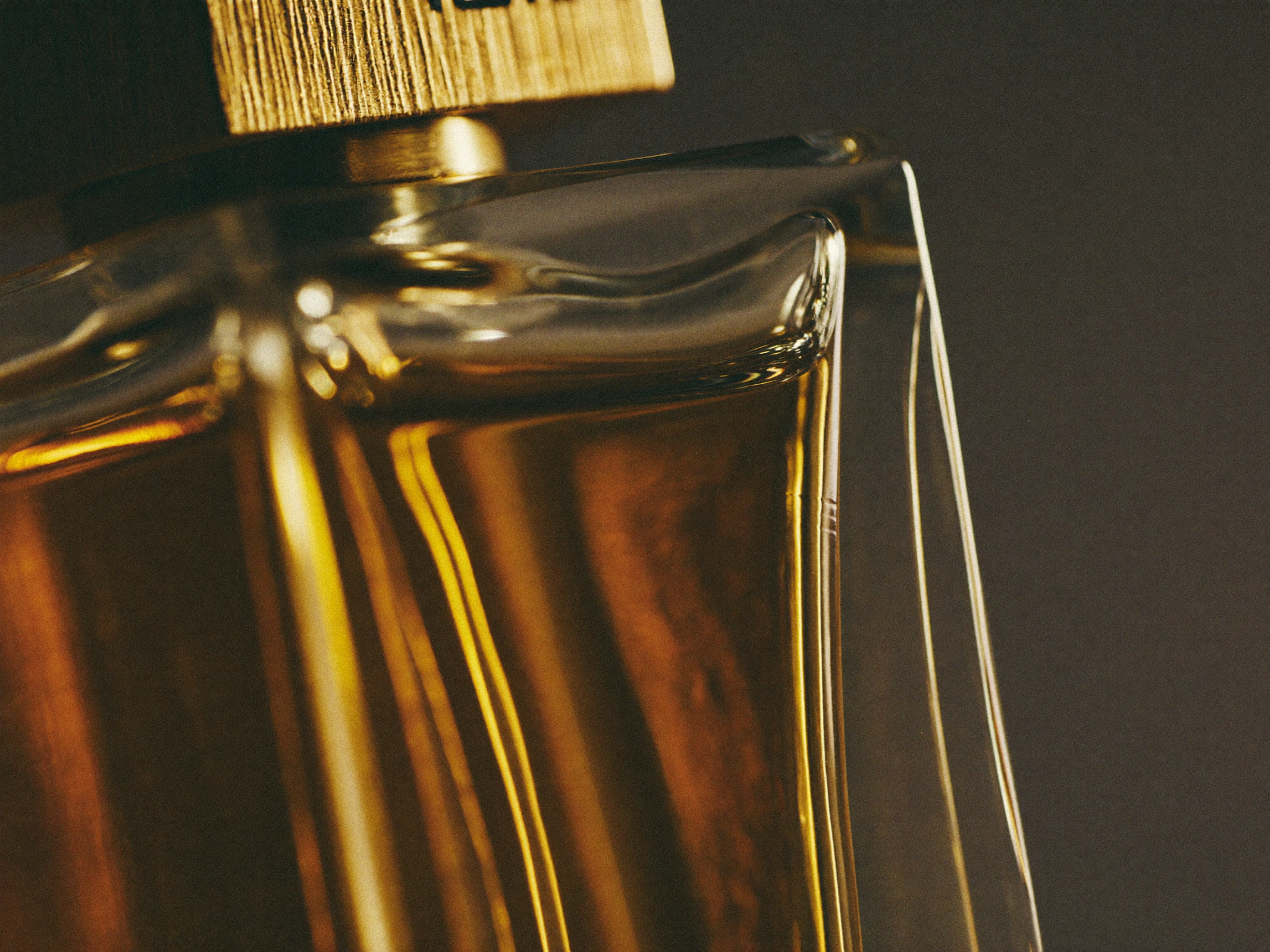 Close-up af ravfarvet parfume der bryder lys inde i en facetteret røget glasflaske